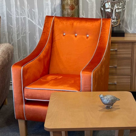 Rathlin comfortable high back contract lounge chair with raked back in orange fabric with contrasting piping and buttons